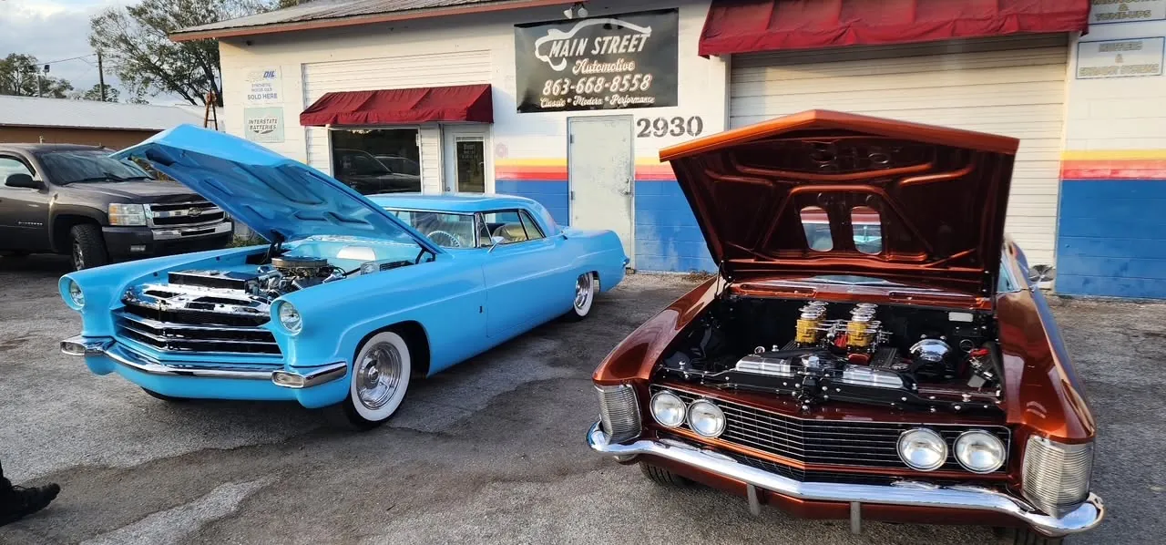 Blue and copper classic cars with open hoods outside Harrell's Main Street Automotive in Lakeland